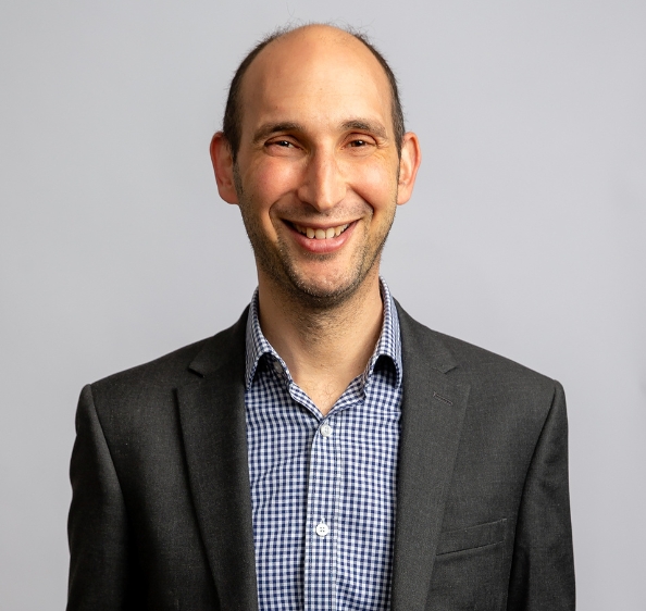 Male in checked shirt and grey jacket smiling at the camera
