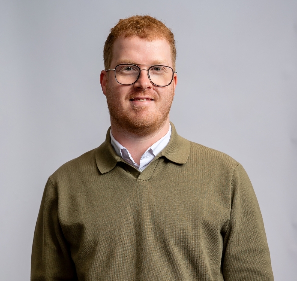 Red Haired male in glasses wearing green jumper over white shirt
