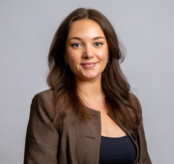 Woman with shoulder length wavy dark hair wearing brown jacket over black top